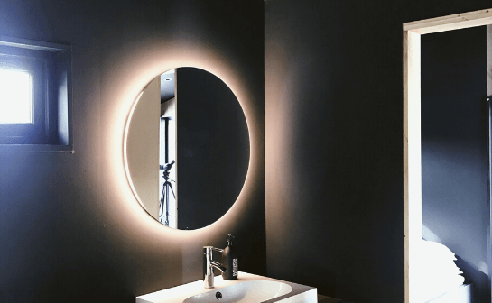 Espelho de um banheiro com fitas de led brancas posicionadas atrás deles, dando uma sensação de aura luminosa