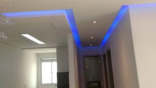 Fitas de led azuis colocadas nas sancas do teto branco, de forma a criar linhas azuladas.